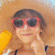child applying sunscreen on face wearing sunglasses and hat