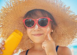 niño aplicándose crema solar en la cara con gafas de sol y sombrero