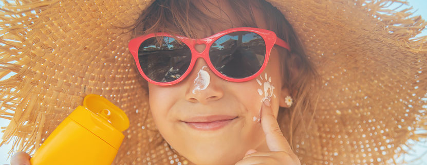 child applying sunscreen on face wearing sunglasses and hat